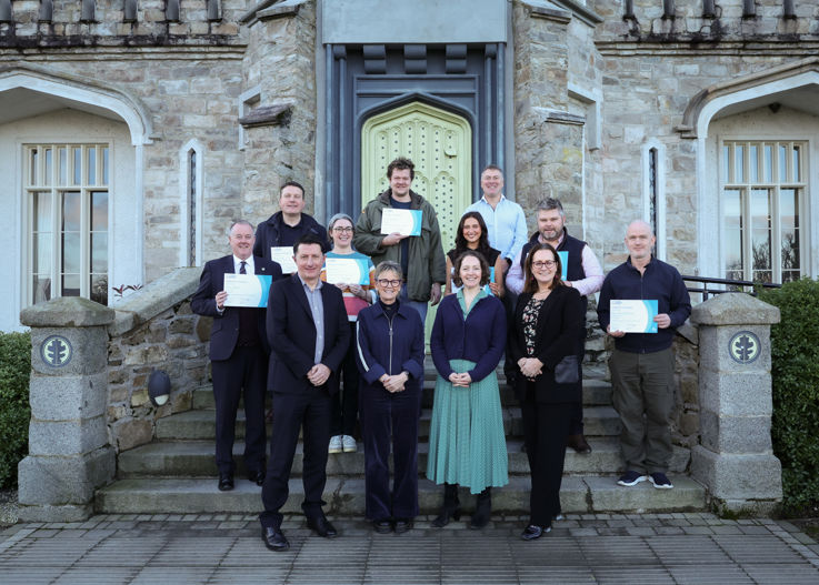 A group of people standing outside Killeavy Castle Estate holding certificates, smiling at the camera.